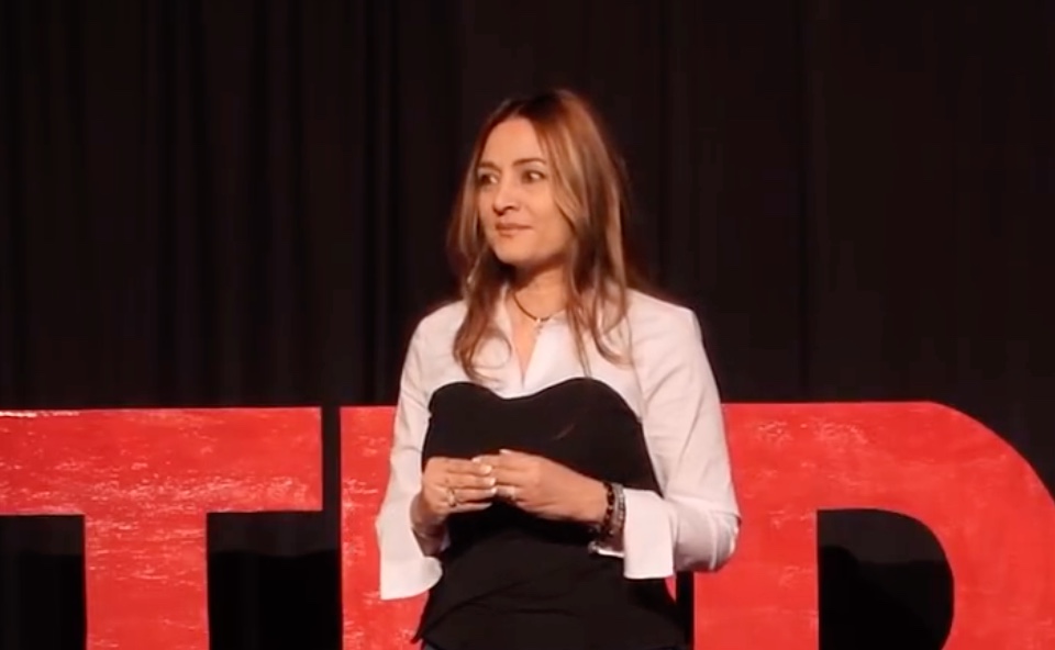 Speaker standing on a TED Talk stage in front of a large red TED logo, delivering a presentation on innovation and ideas worth spreading